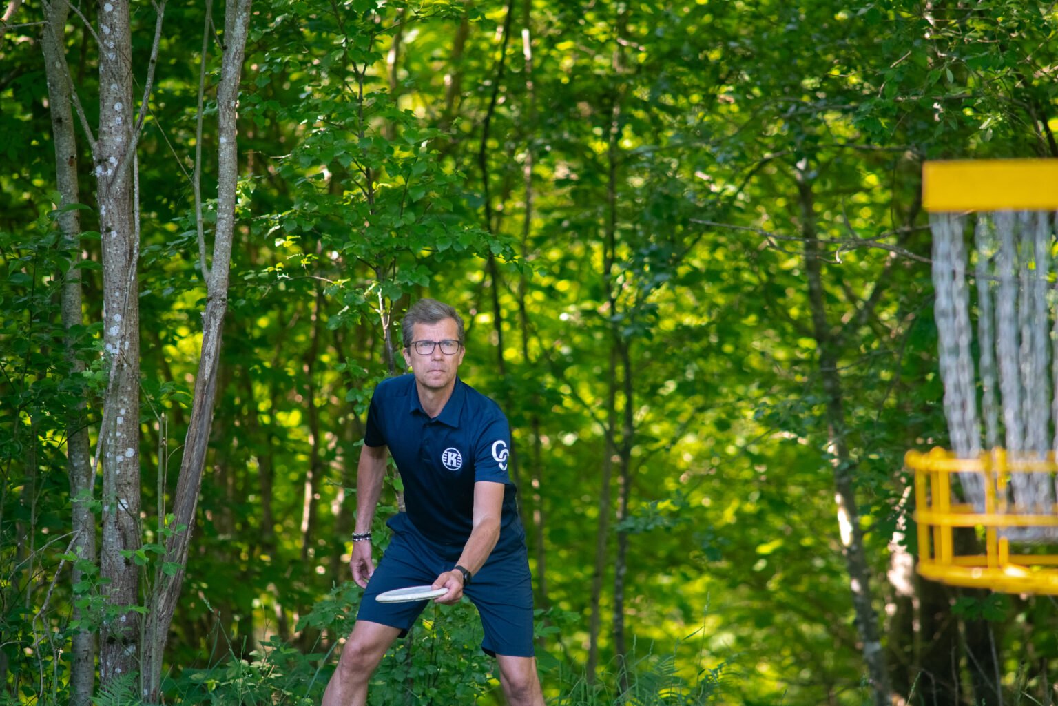 Discgolfspelare med disc i skogen, korg i förgrunden